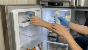 Heavy mineral scale and calcium buildup choking a refrigerator ice maker assembly unit being inspected by a technician.